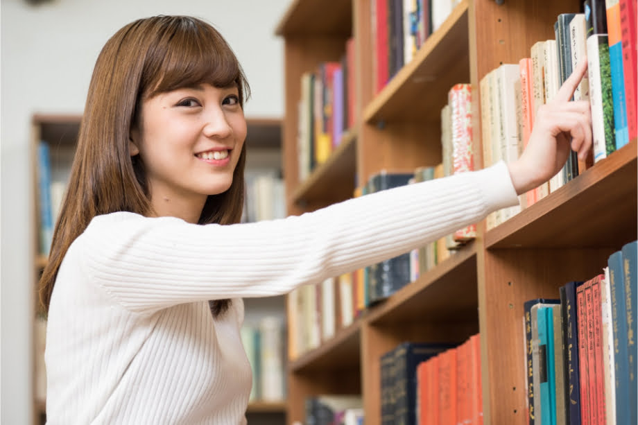 本棚に手をかけて笑う女性